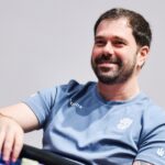 Felipe Boianovsky sorri de camiseta azul-clara, com a mão esquerda sobre as fichas na beira de uma mesa de poker