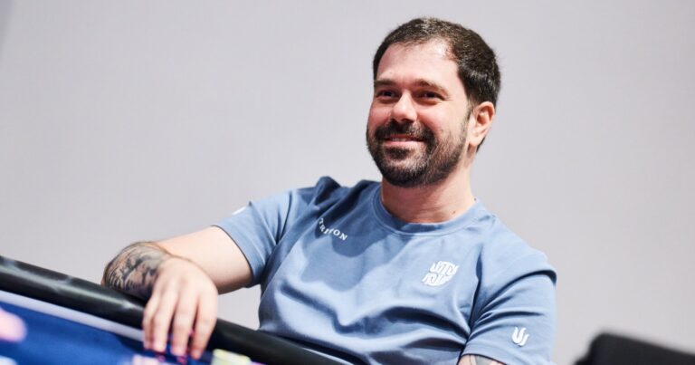 Felipe Boianovsky sorri de camiseta azul-clara, com a mão esquerda sobre as fichas na beira de uma mesa de poker