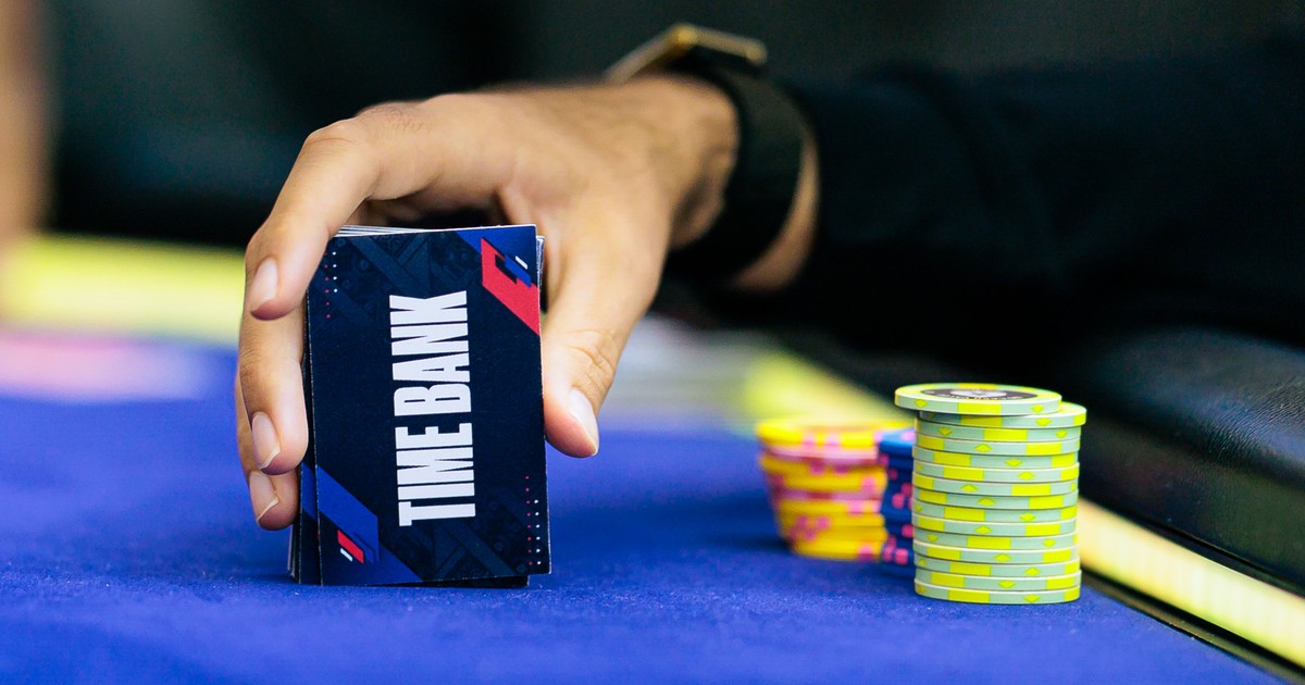Mão de jogador segurando cartões de time bank ao lado das fichas em uma mesa de torneio de poker
