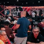 Salão do Joker's Poker Tour com jogadores nas mesas e painel CASH GAME com o logo do JPT