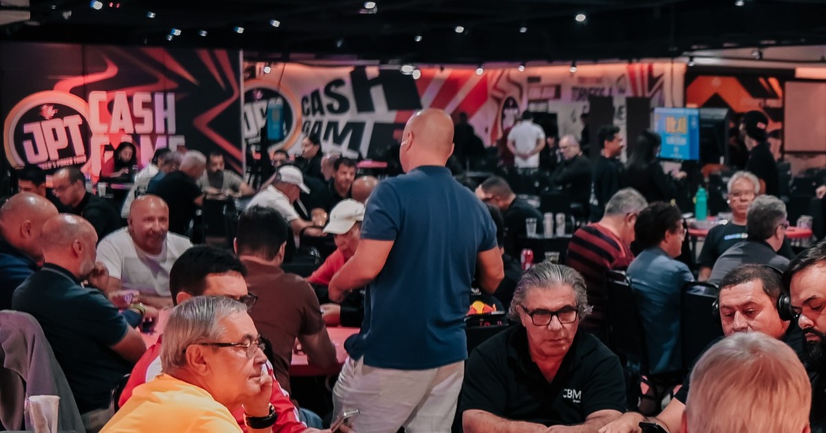 Salão do Joker's Poker Tour com jogadores nas mesas e painel CASH GAME com o logo do JPT