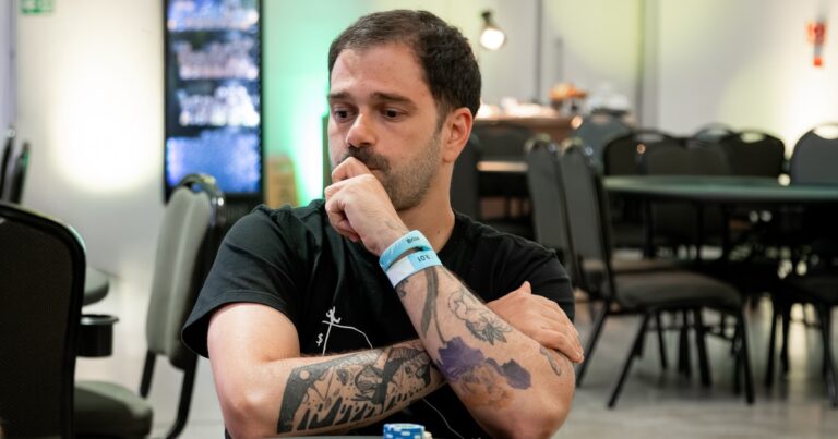 Felipe Boianovsky, de camiseta preta, apoia o queixo na mão e cruza os braços tatuados sobre a mesa de um torneio do BSOP